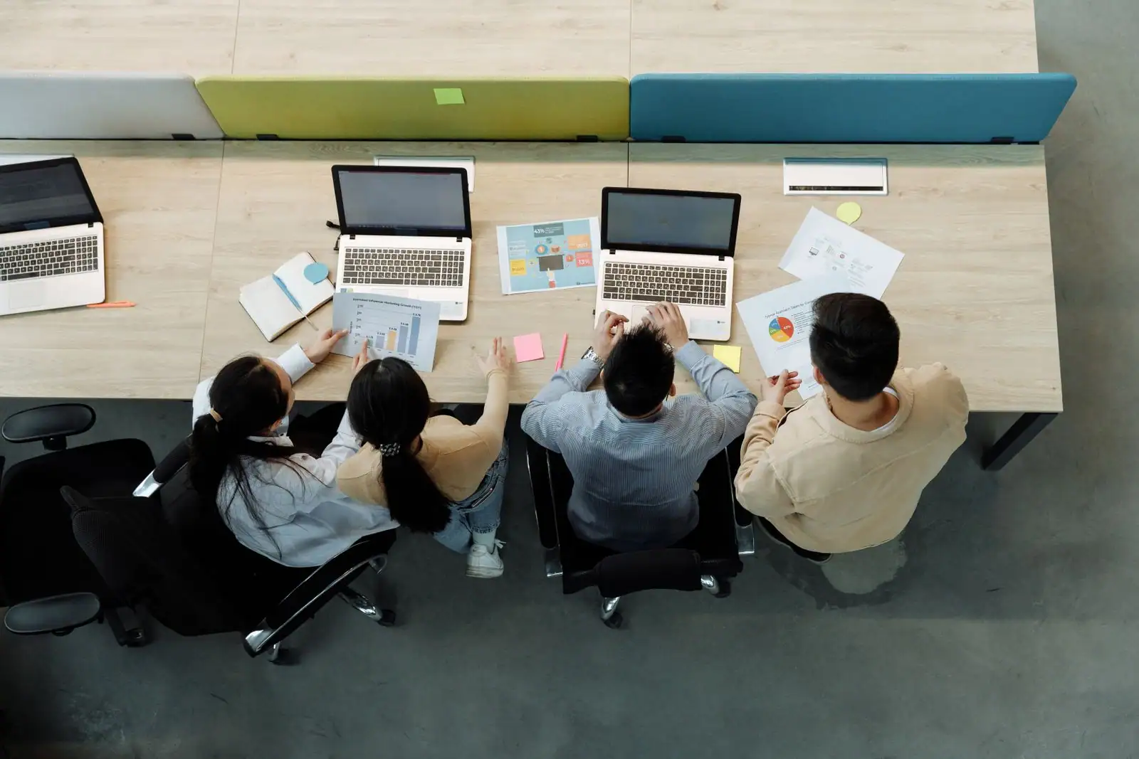 Quatre collègues assis à un bureau partagé, ordinateurs portables et documents devant eux.