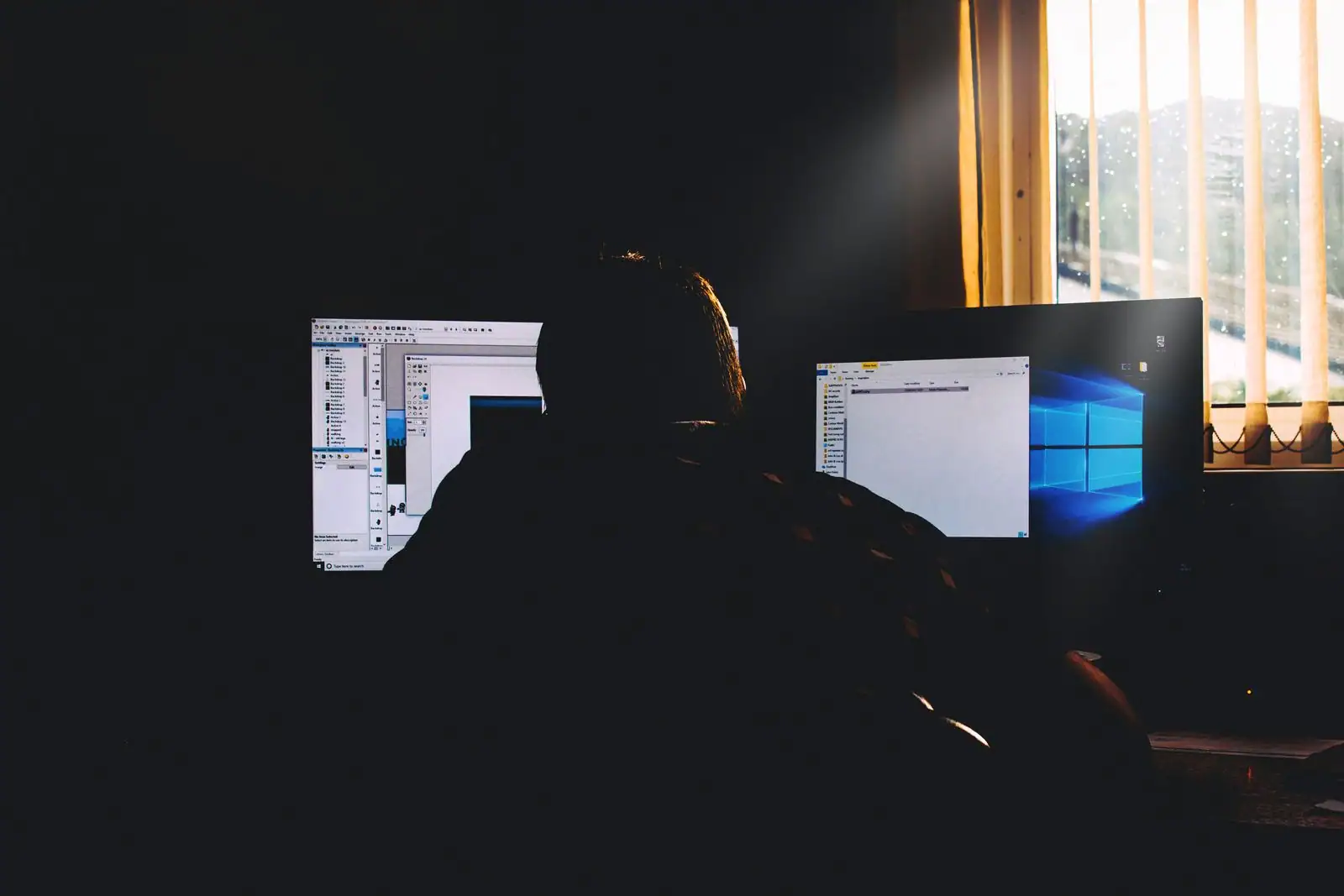 Personne devant deux écrans d'ordinateur affichant des fenêtres et le bureau d'un système d'exploitation.