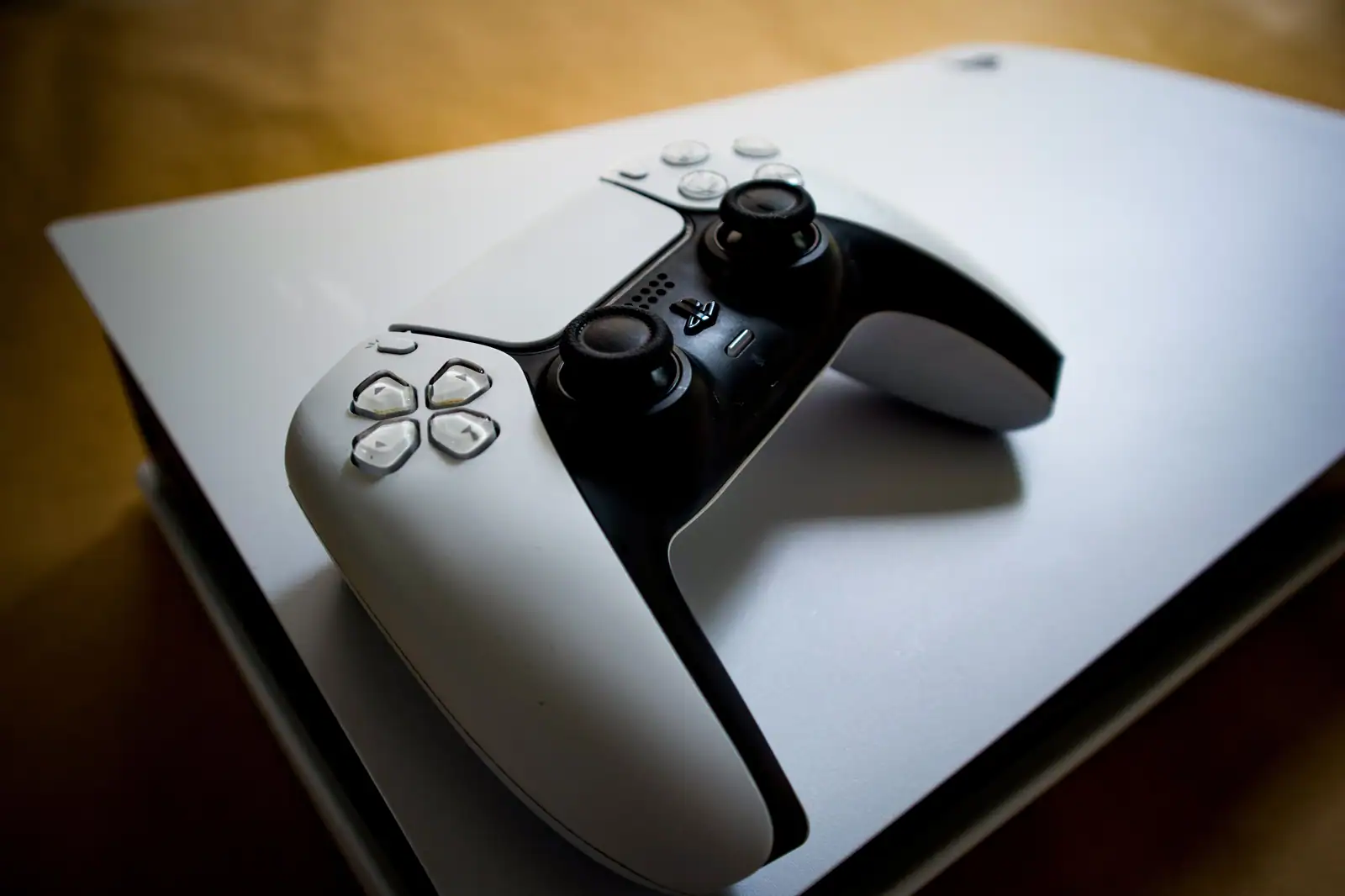 Manette de PlayStation 5 blanche et noire posée sur la console, éclairée par une lumière chaude.