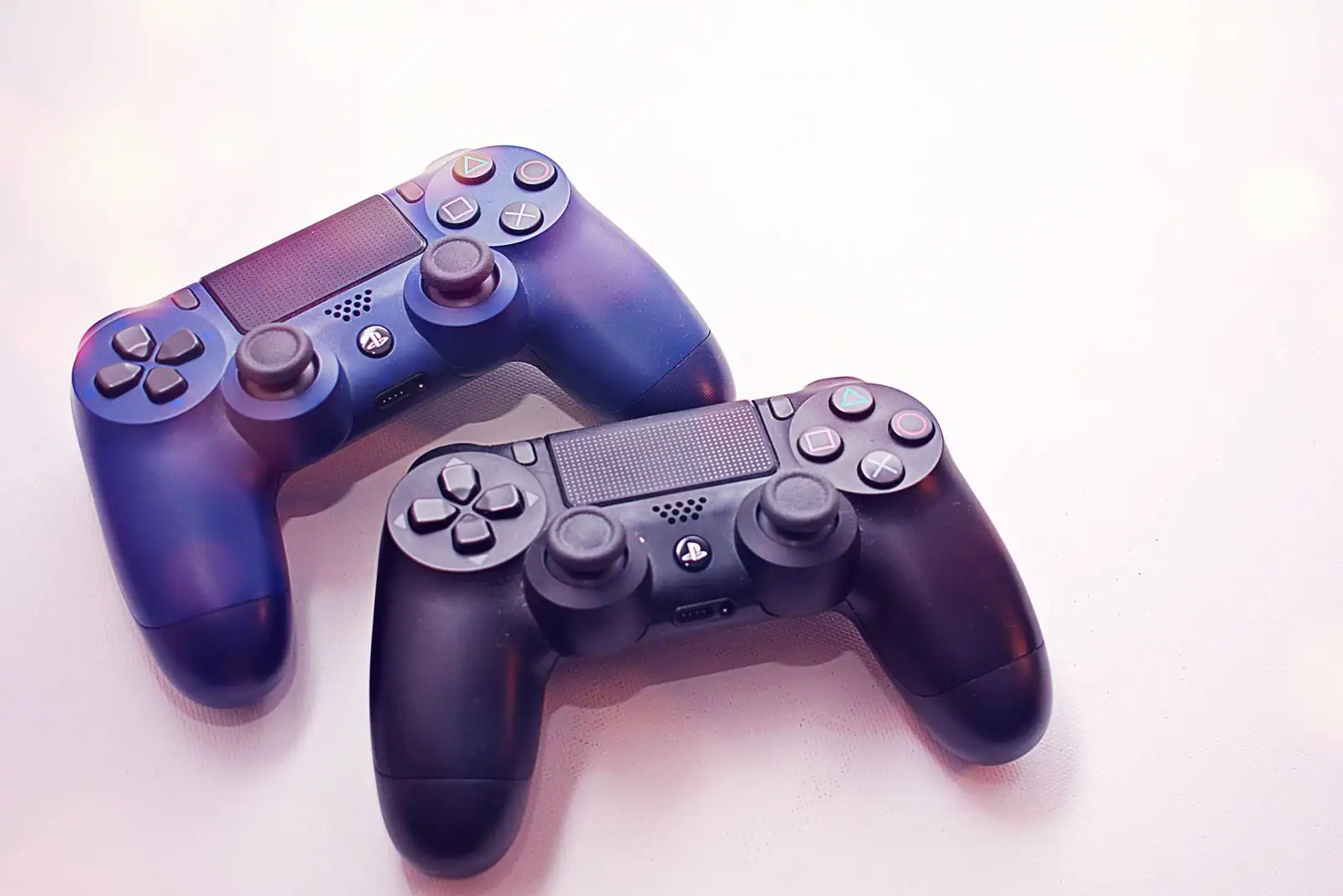 Deux manettes de PlayStation, l'une bleutée et l'autre noire, posées côte à côte sur une surface blanche.