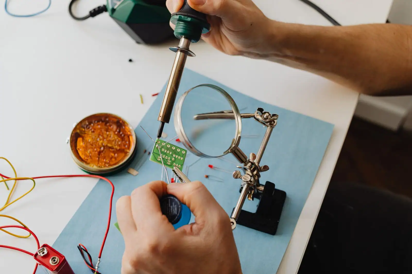 Réparation de composants électroniques au fer à souder sur un établi, carte à circuit imprimé maintenue sous une loupe