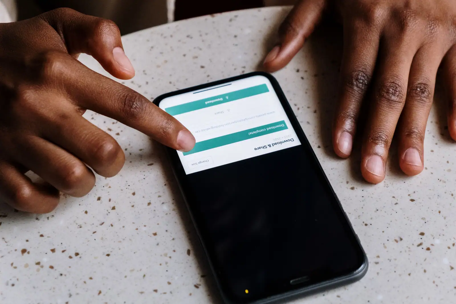 Doigt au-dessus d'un smartphone posé sur une table, écran affichant un téléchargement terminé.
