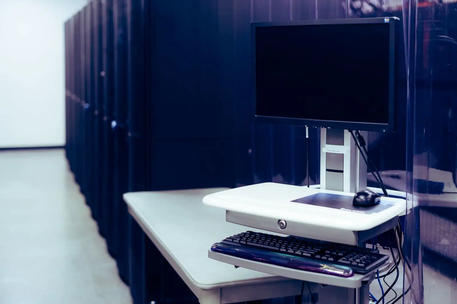 Salle serveurs d'un centre d'hébergement, avec un poste informatique devant des baies alignées
