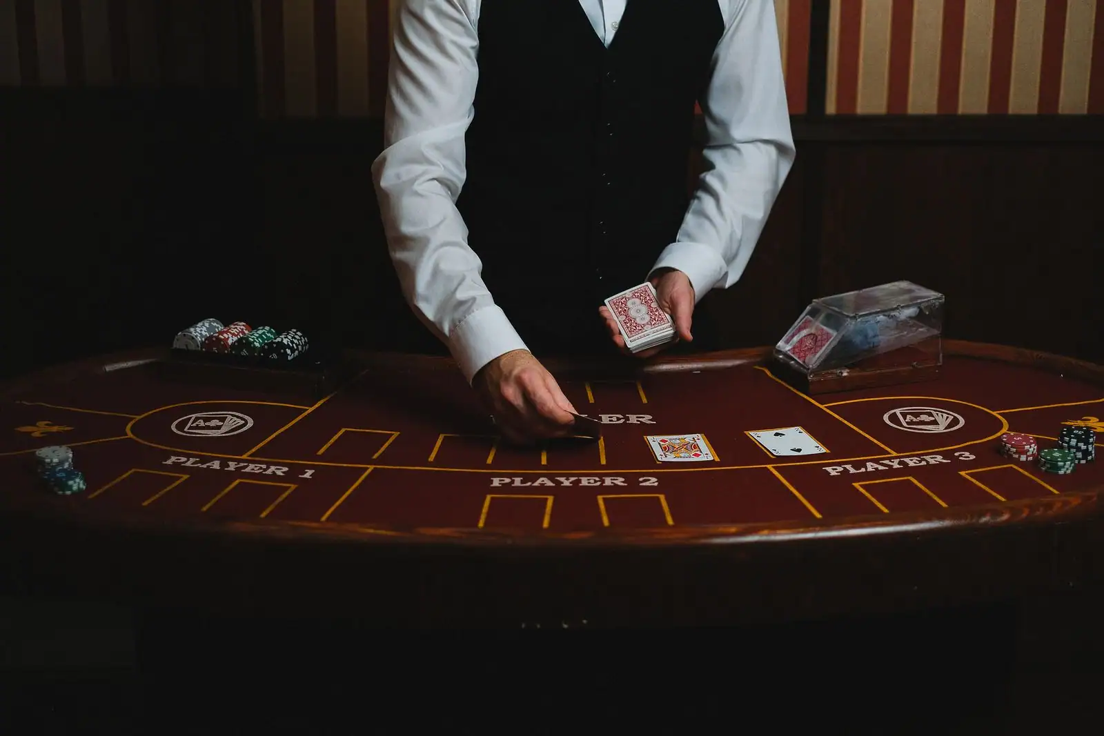 Un croupier en gilet distribue des cartes sur le tapis d'une table de casino bordée de piles de jetons.