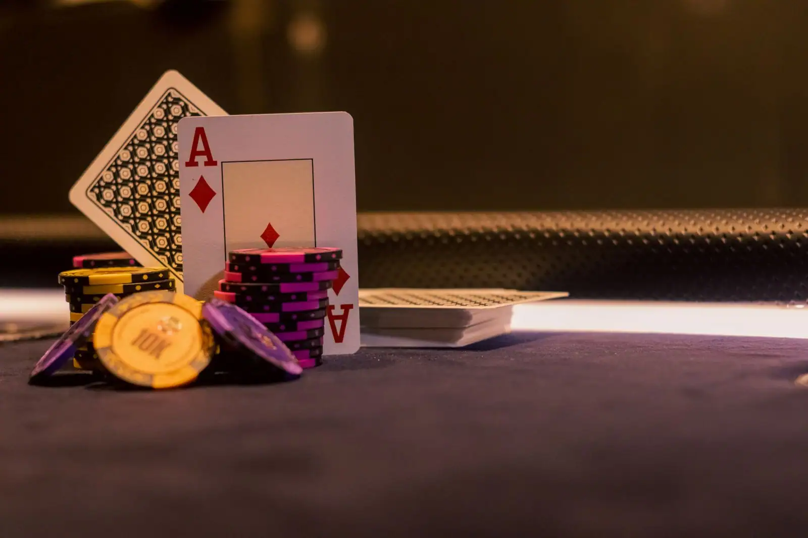Carte d'as, jetons de casino colorés et jeu de cartes posés sur une table de jeu sombre.