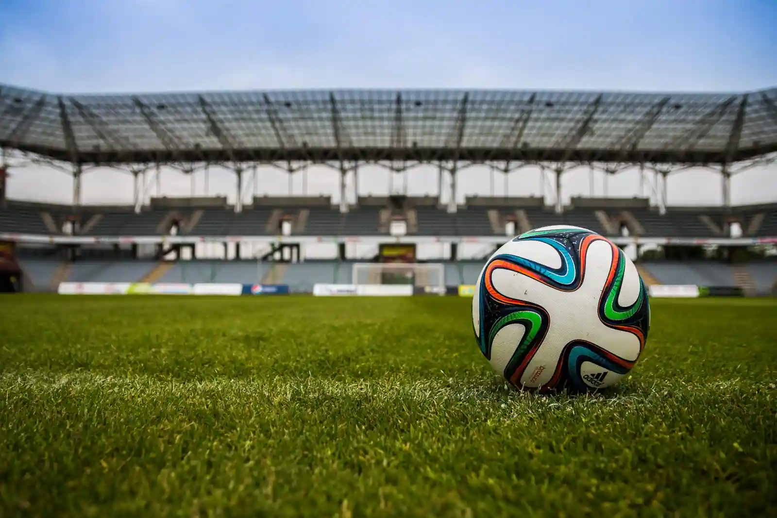 Ballon de football posé sur la pelouse d'un stade, devant des gradins vides avant une rencontre.