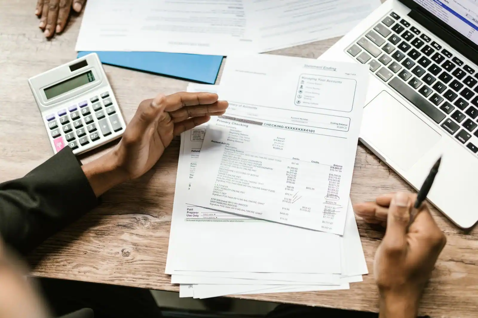 Personne examinant des documents chiffrés avec une calculatrice, sur un bureau de travail