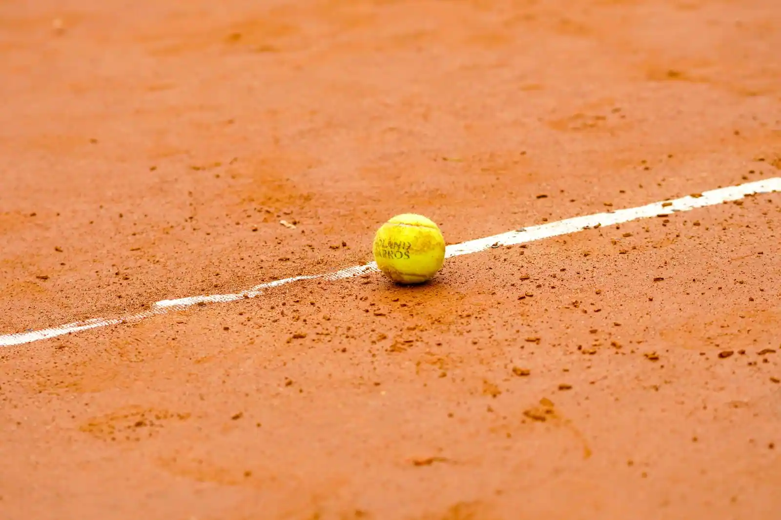 Balle de tennis Roland-Garros posée sur la ligne d'un court en terre battue.