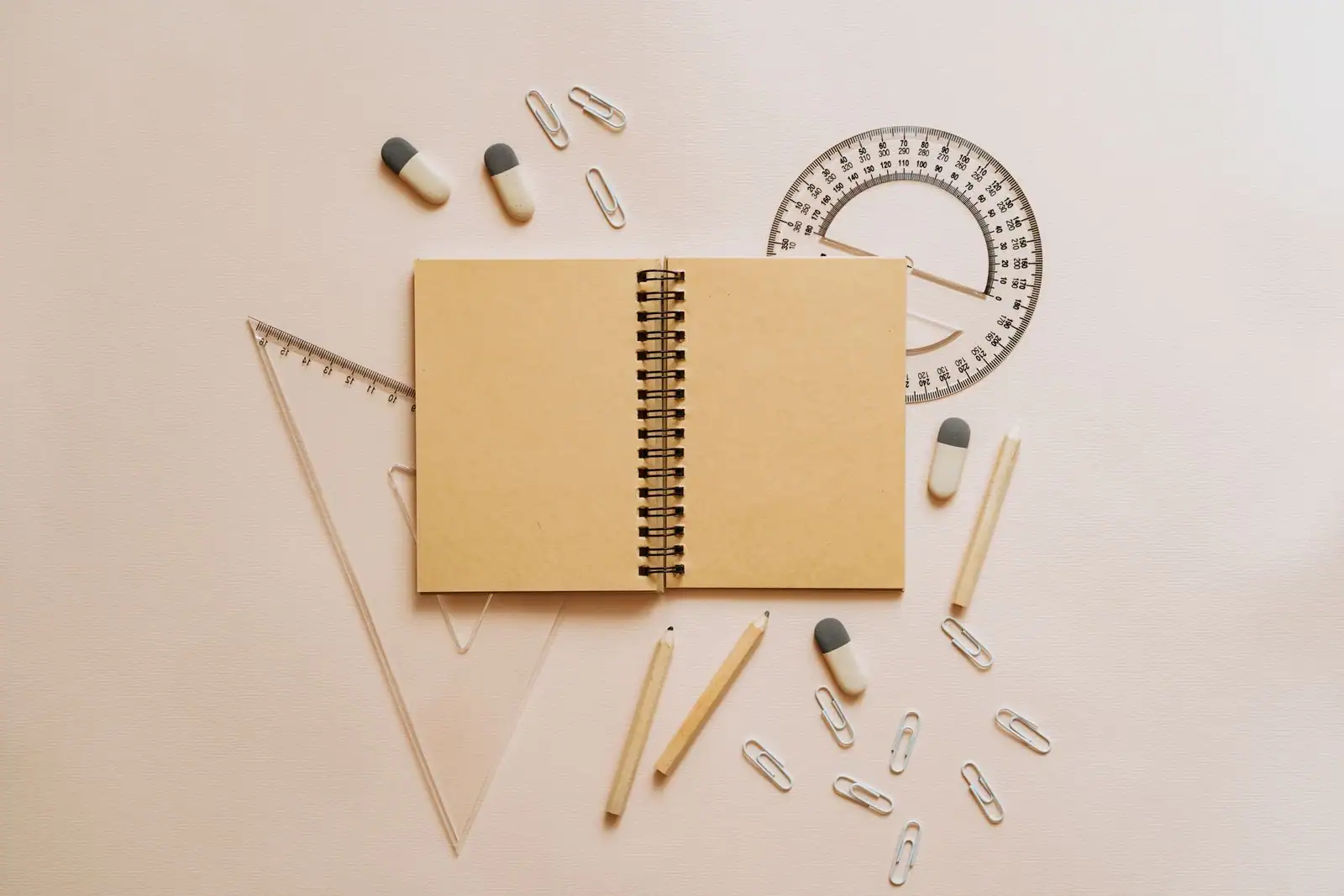 Carnet à spirale ouvert et vierge entouré d'un rapporteur, d'une équerre, de crayons et de trombones sur un fond clair.