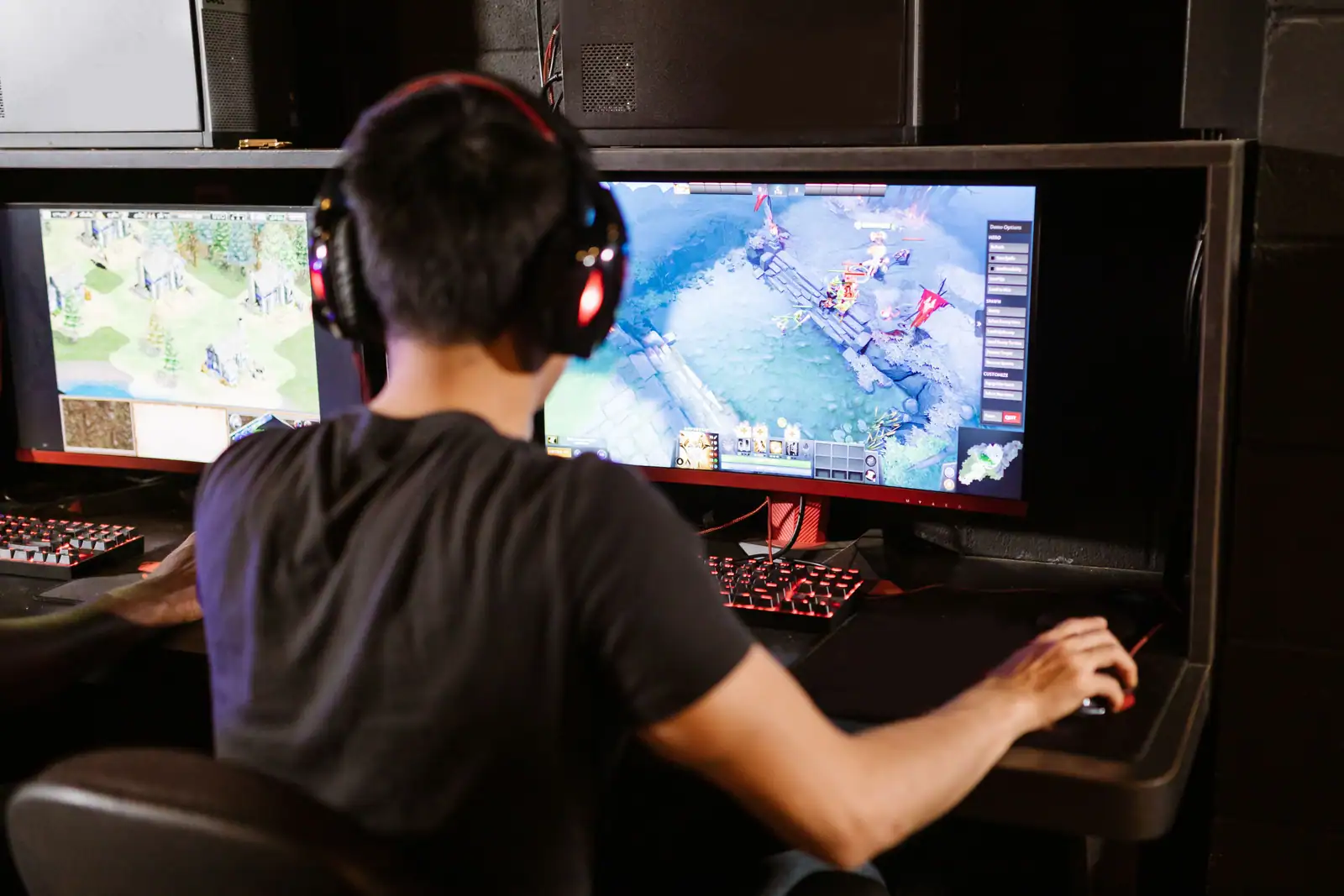 Joueur de dos, casque sur les oreilles, devant deux écrans affichant un jeu vidéo en vue isométrique.