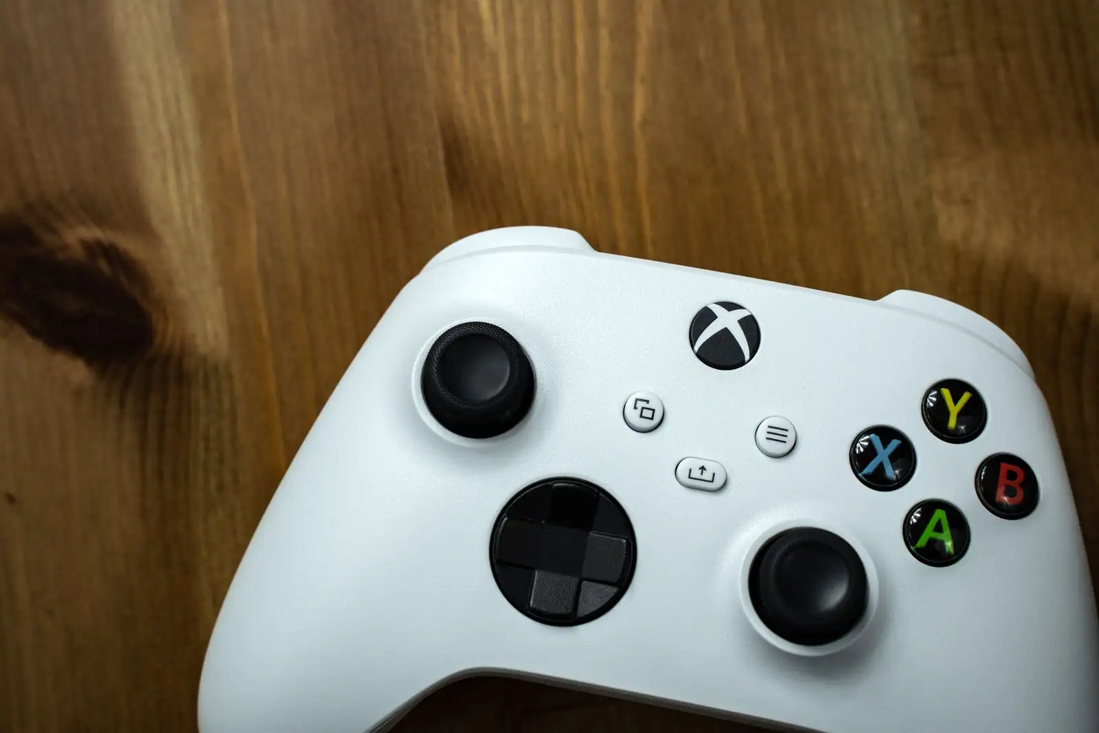 Manette Xbox blanche posée sur un plan de travail en bois, boutons colorés et logo bien visibles
