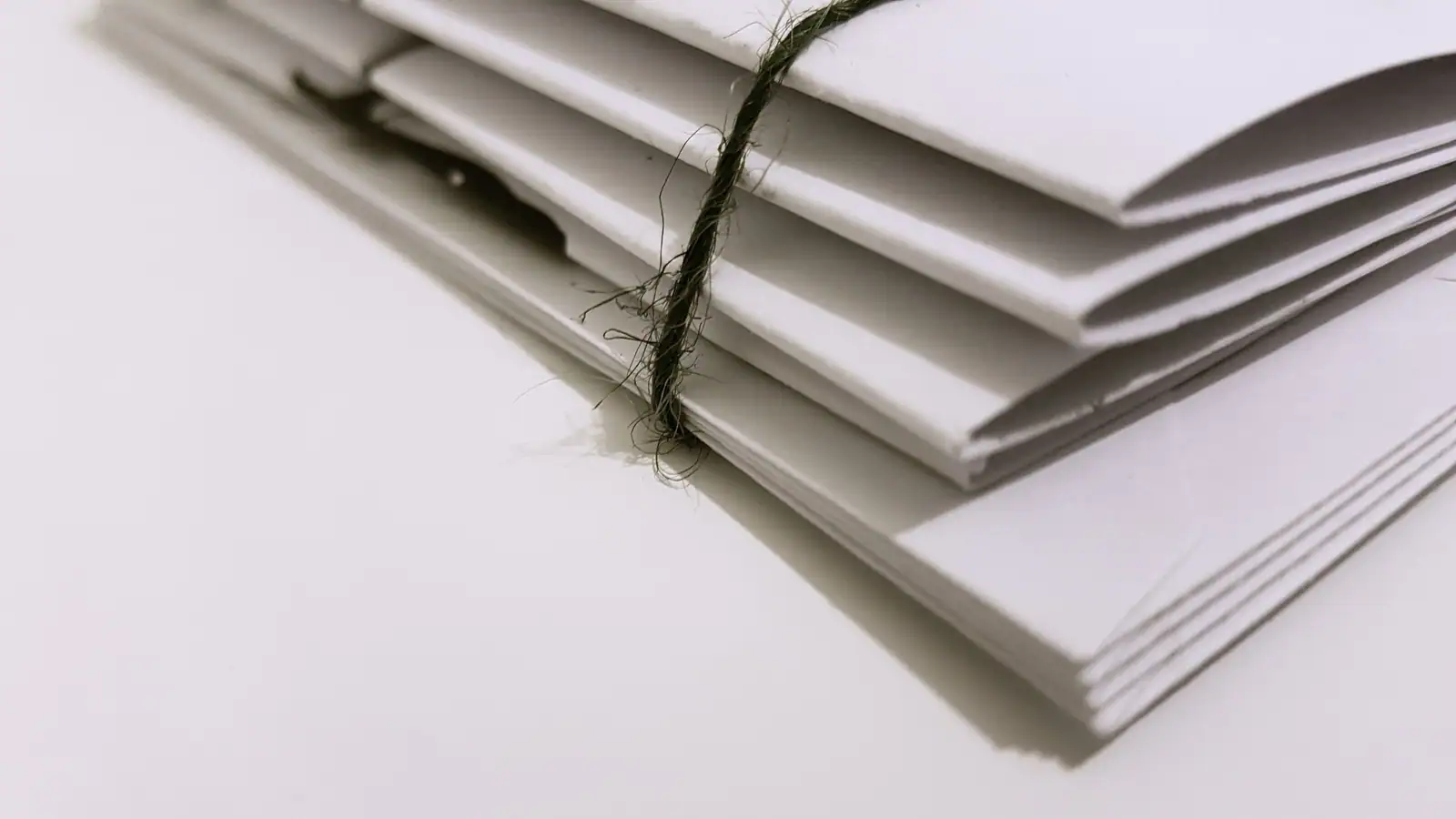 Petit paquet d'enveloppes blanches liées par une ficelle, posé sur une surface claire.