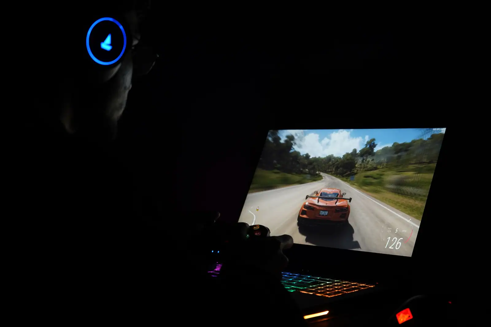Écran d'ordinateur portable affichant une séquence de jeu de course automobile, dans une pièce sombre.