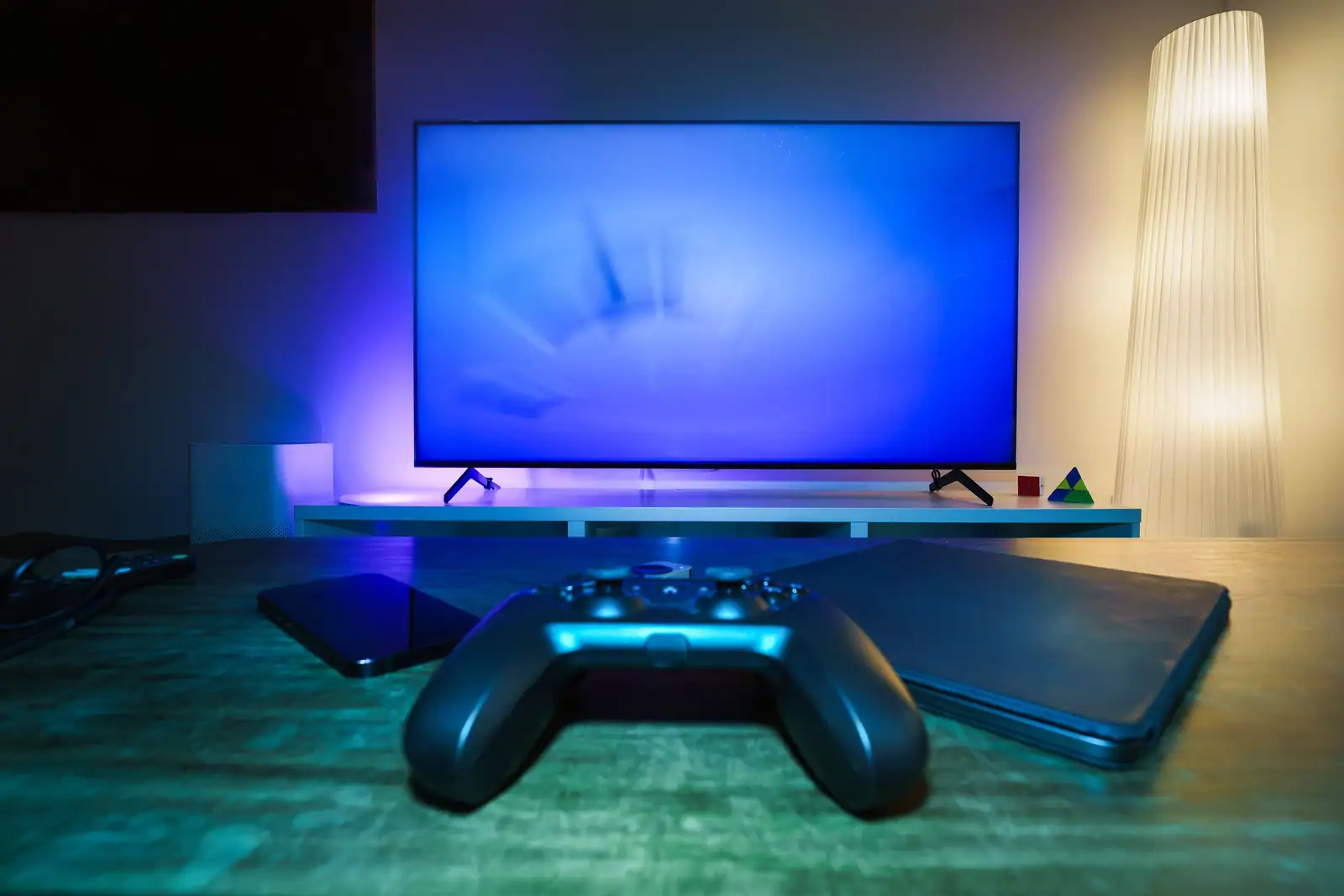 Manette de jeu posée devant un téléviseur allumé dans un salon éclairé, console visible à côté