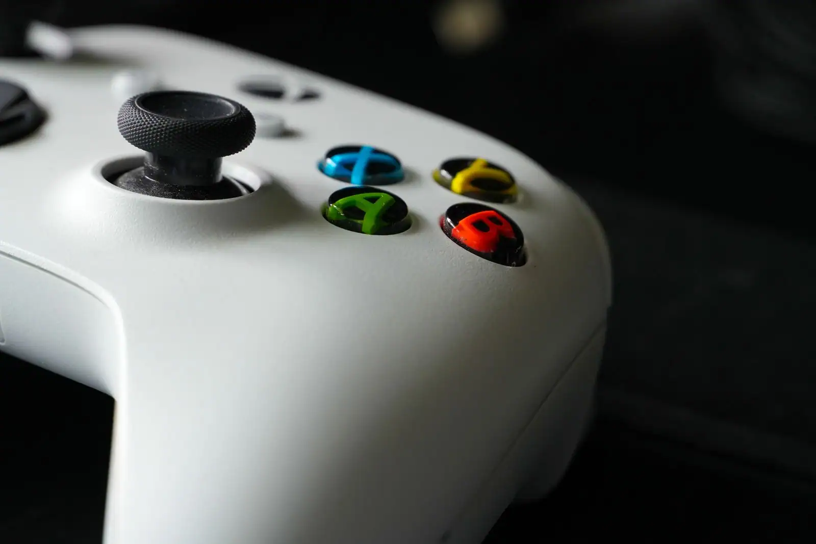 Gros plan sur une manette Xbox blanche, aux boutons colorés A, B, X et Y, sur fond sombre.