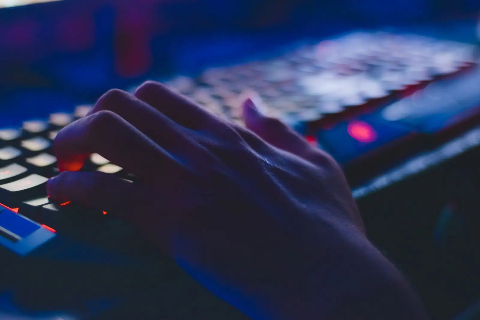 Main tapant sur un clavier rétroéclairé dans la pénombre, pour illustrer la saisie sécurisée d'un mot de passe
