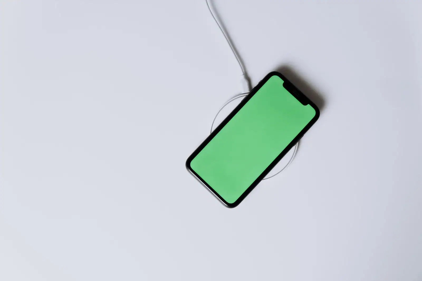Smartphone posé à plat sur un chargeur à induction, câble d'alimentation visible, sur une surface blanche
