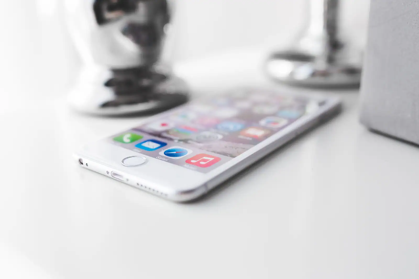 Un iPhone posé sur une surface blanche, avec l'écran d'accueil et ses applications visibles.