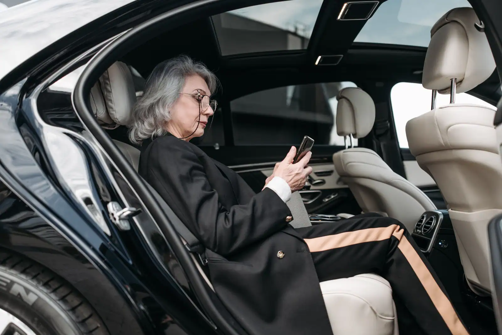 Personne assise à l'arrière d'une berline, portière ouverte, qui consulte son smartphone.
